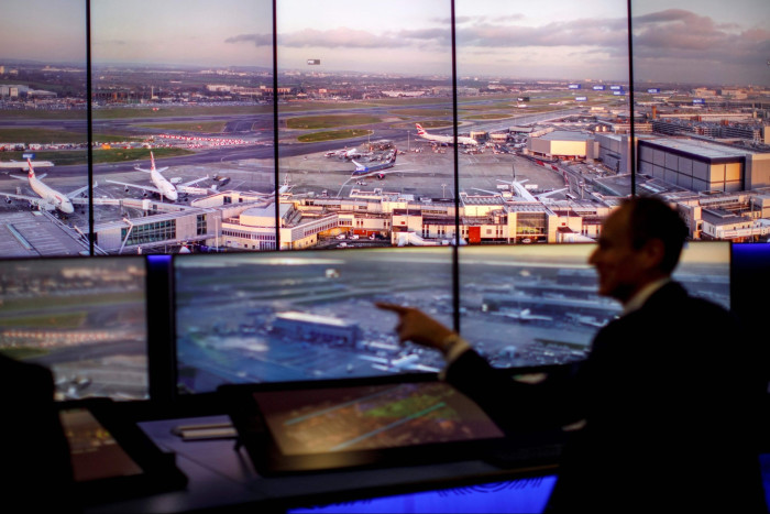 An air traffic control engineer pointing to one of the panoramic screens displaying views of the runways