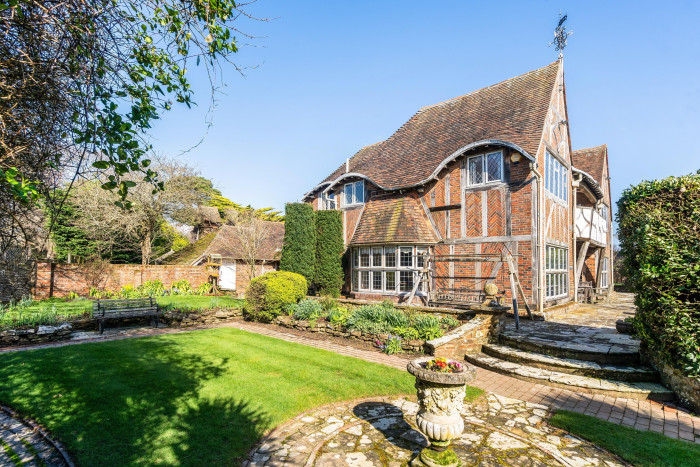 English countryside home with a classic Tudor architecture, including white and brown timber framing, set in a vibrant garden with neatly trimmed hedges and a vintage sundial on a sunny day