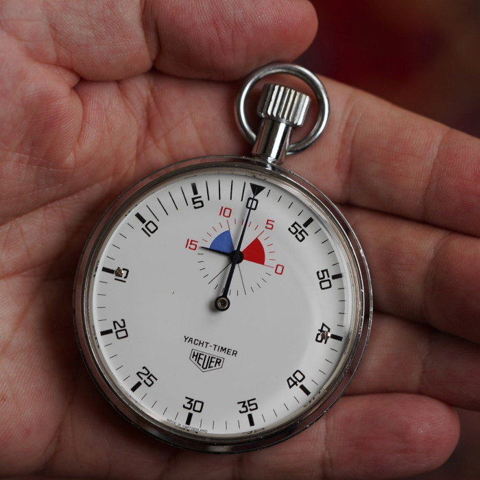 a vintage-style stopwatch with a round metal case held in hand. The crown and the loop are located at the top