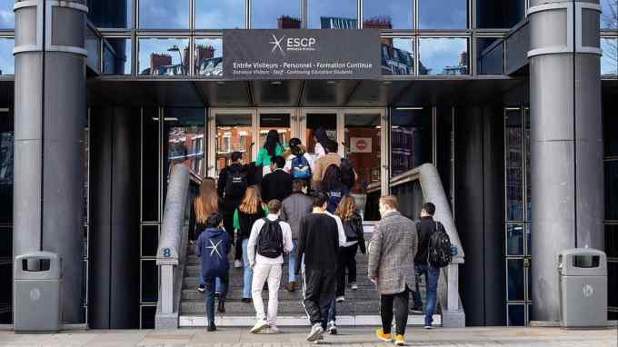 a group of adult students climbing up the stairs to the entrance of a campus