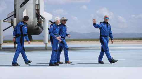 Four individuals wearing blue flight suits walking away from a spacecraft after what appears to be a successful space mission or landing