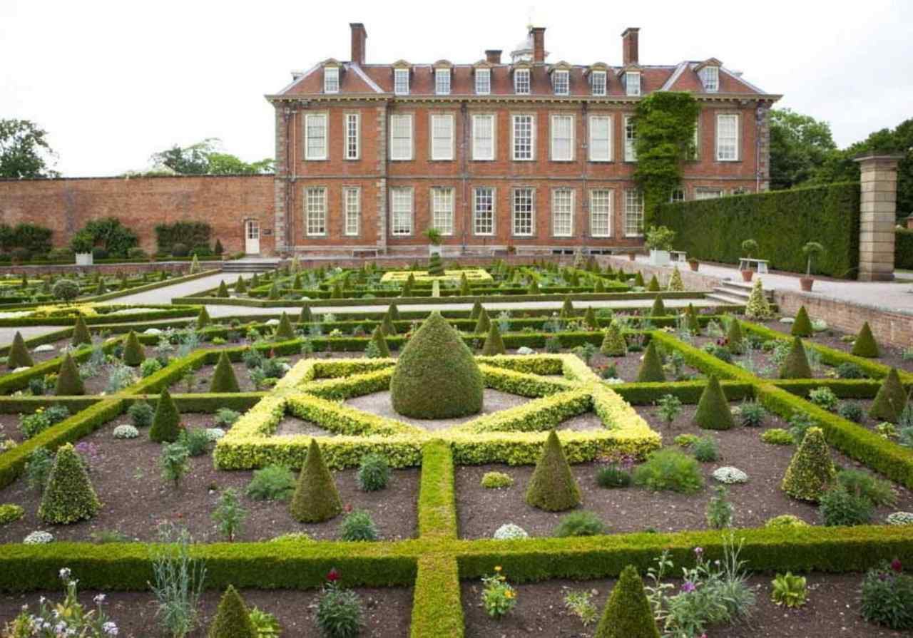 A grand red-brick mansion has formal geometric gardens at the front