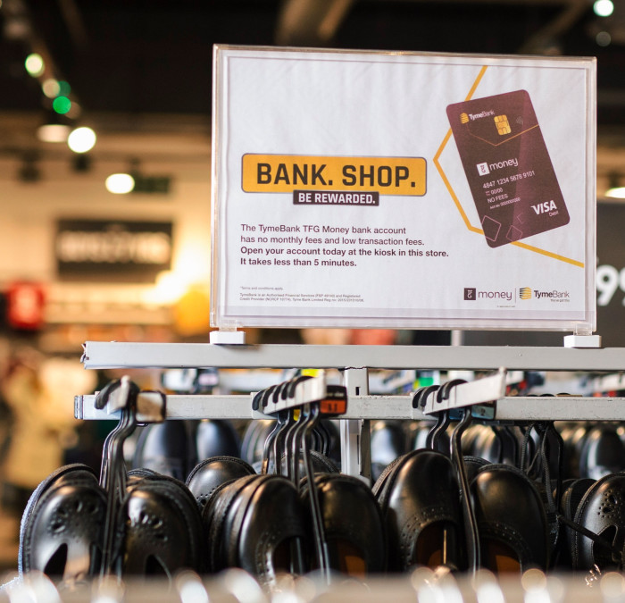 A Tyme Bank advertisement hangs over a shoe rack in a department store.