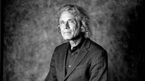 Black and white portrait of Steven Pinker, who has shoulder length hair, wearing an open collared shirt and suit jacket