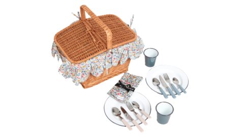 a wicker picnic basket. Beside it are utensils, napkins, plates and cups