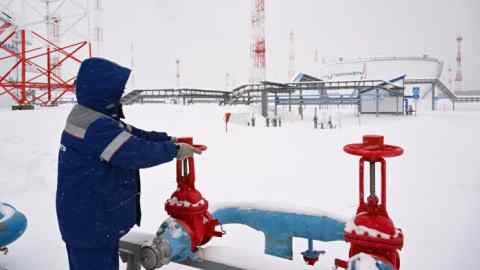 A person turns a metal valve outside an oil refinery