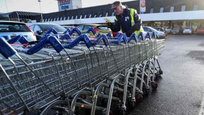 An employee pushes shopping trolleys back to the store at the Tesco Basildon Pitsea Extra supermarket, operated by Tesco Plc