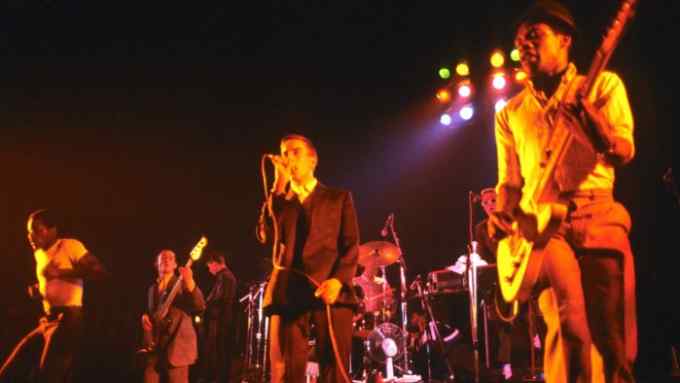 A pop group perform on stage with an electric guitarist in the foreground