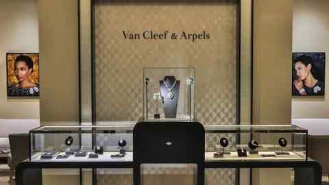 A Van Cleef & Arpels exhibit showcasing a modern design with geometric patterns on the walls, a display table with jewelry pieces, and decorative portraits of models wearing the jewelry
