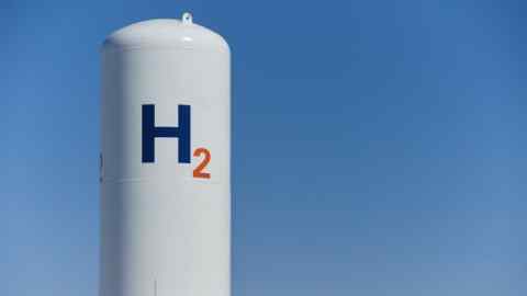 A large white cylindrical tank with the symbol “H2” written in blue and orange, set against a clear blue sky