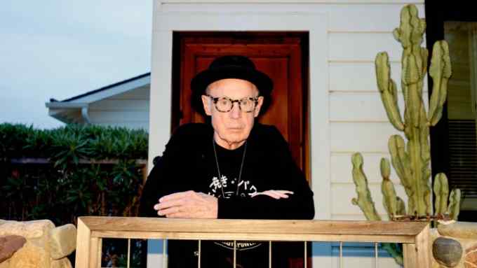 A man in a black hat leans on a garden gate by a cactus