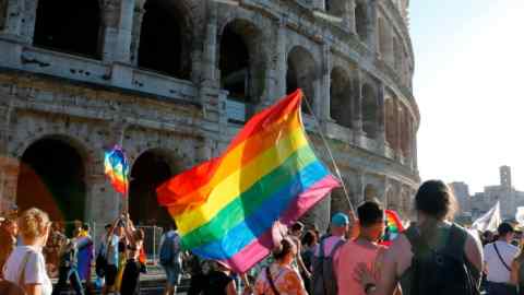 Attendees at last year’s Rome Pride parade walking past the Colosseum waving a large rainbow flag