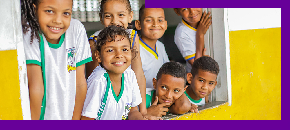 Imagem mostra menina de uniforme escolar sorrindo segurando um tablet onde se vê o logotipo do Profuturo Aula Digital