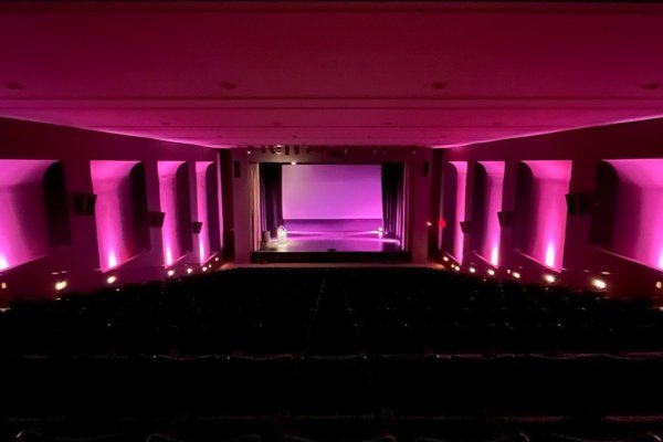 View of an auditorium bathed in pink light, facing a stage with movie screen. 