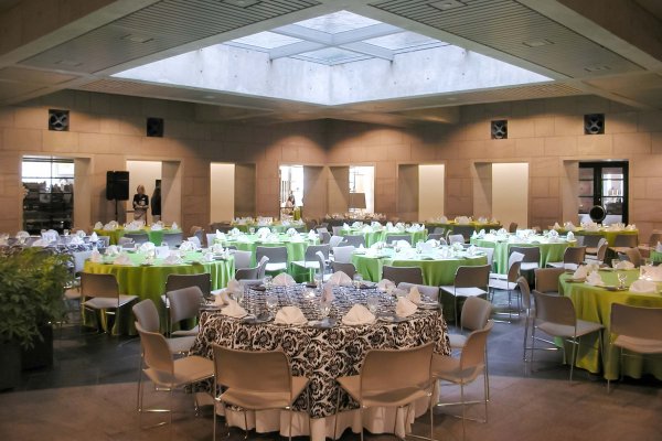 Formal dinner tables in an open space with light from the floor above, and rectangular openings on the far wall. 