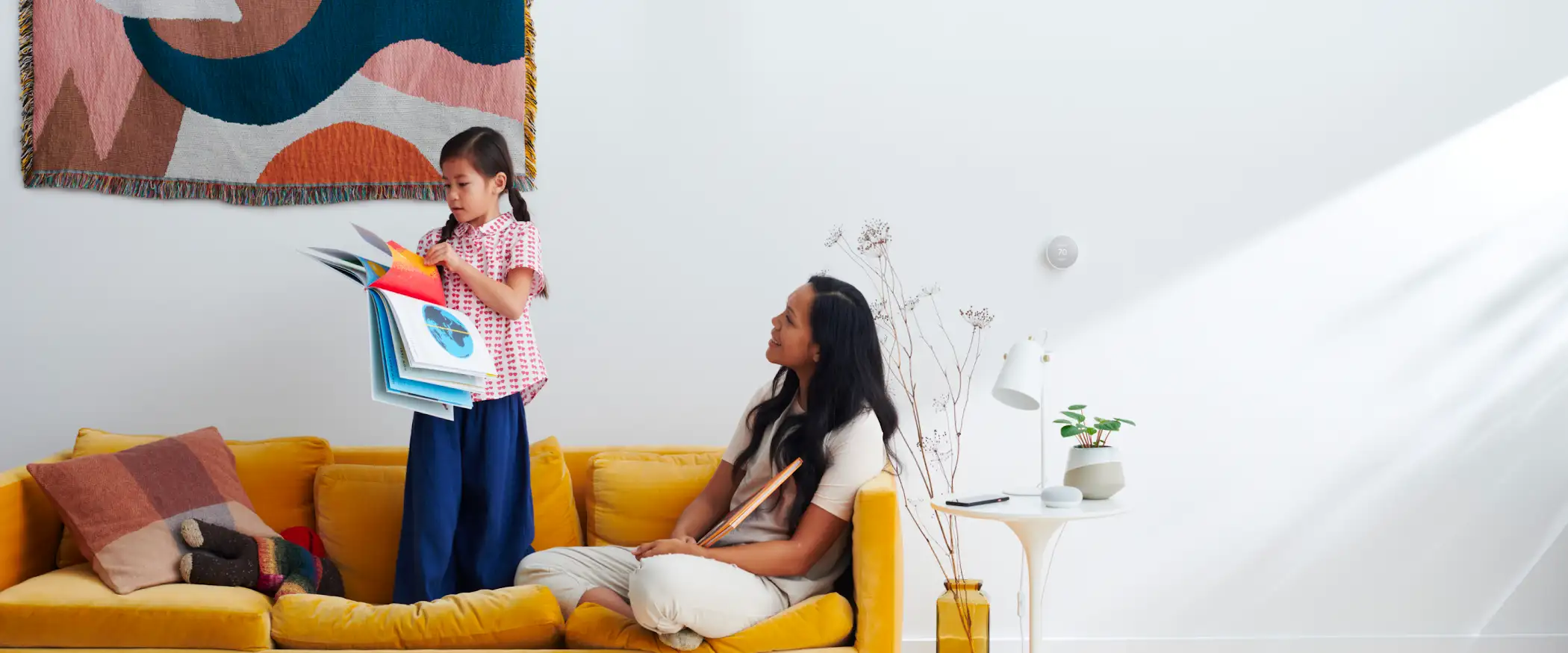 A woman sitting on a yellow couch with her child and a book