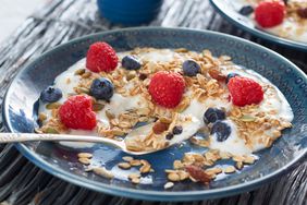 Breakfast of yogurt topped with granola, blueberries, raspberries and maple syrup served on a plate