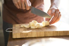 person cutting banana on cutting board with sharp knife