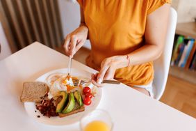 Person sits down to eat eggs, avocado, toast, orange juice and tomatoes. 