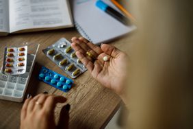 Unrecognizable person sitting at desk, taking pills out of their packages, putting on the palm of her hand