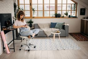 Shot of a young woman sitting in an office chair, using a smartphone in her small apartment.