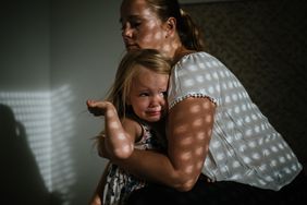 mom hugging a scared and tearful daughter in a dark room 