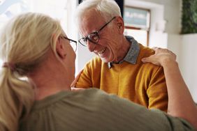 Closeup of a senior man laughing while greeting a female friend with a hug during a visit together