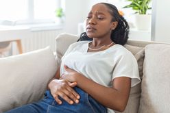 Woman holding her stomach while sitting in the couch looking uncomfortable