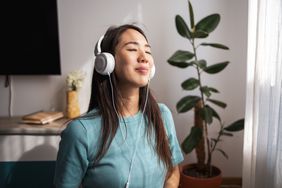 Asian woman wearing white over-ear headphones at home, looking happy and relaxed