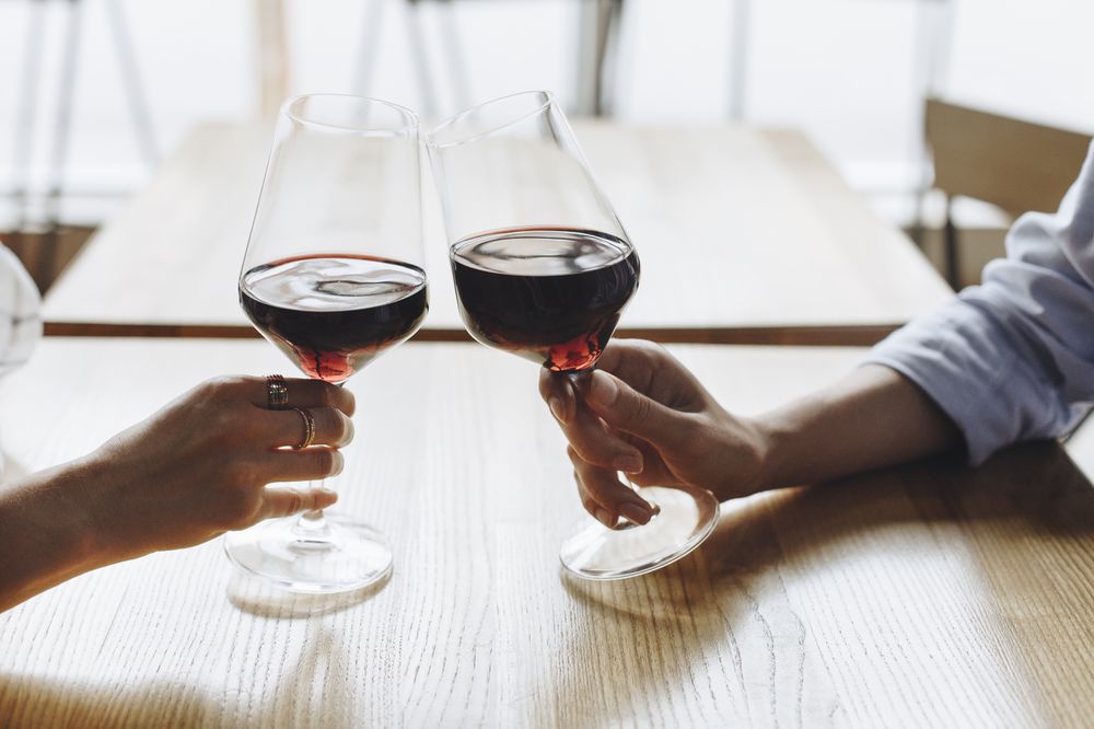 Two people hold glasses of red wine at the dinner table.