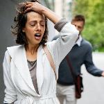 A couple fighting outside, the woman looking distressed and walking away while the man follows her.