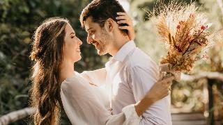 A couple embracing each other closely, the woman holding a bouquet in her free hand.