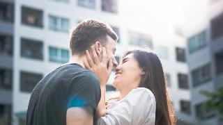 A close shot of a couple standing close, their noses together, the woman holding the man's face.