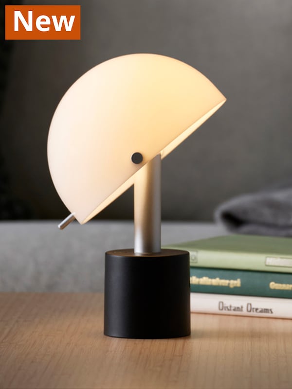 A white/black NÖDMAST LED portable lamp, battery operated sitting on top of a brown table.