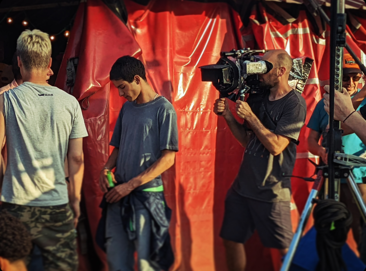 Cinematographer Benjamin Roux with a camera on his shoulder shooting actors in front of a red tent on the set of 'Block Pass'