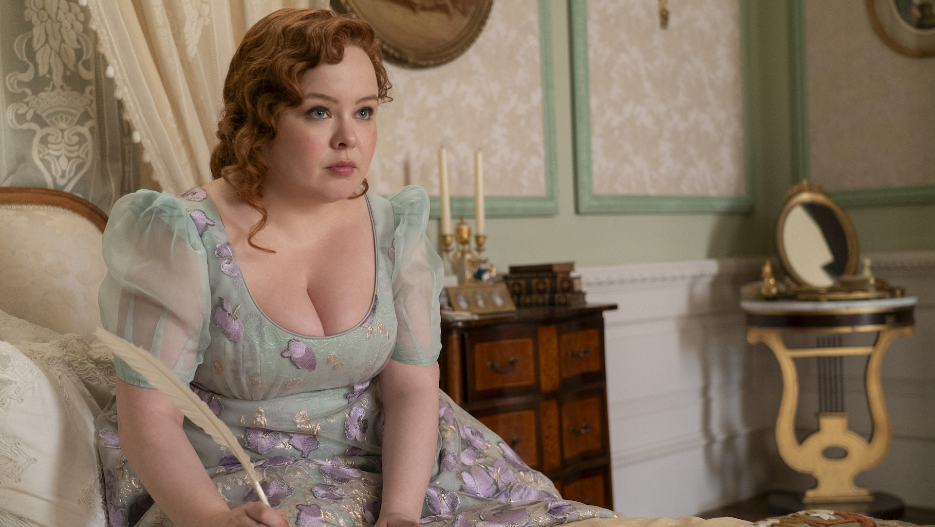 A woman in a Regency Era floral dress, writing with a quill; Nicola Coughlan in 'Bridgerton' Season 3