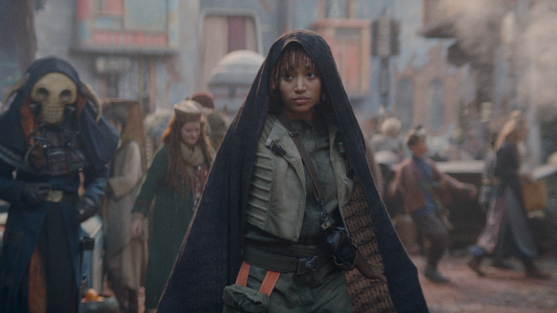 A female presenting individual in a black cloak on the streets of an alien planet; still from 'The Acolyte'