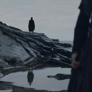 An image from 'The Acolyte' of The Stranger (Manny Jacinto) standing with his back to the camera, reflected in a pool of water. A figure stands in the foreground holding a knife.