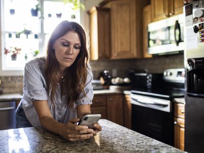 A woman stands at a kitchen counter looking at her smartphone