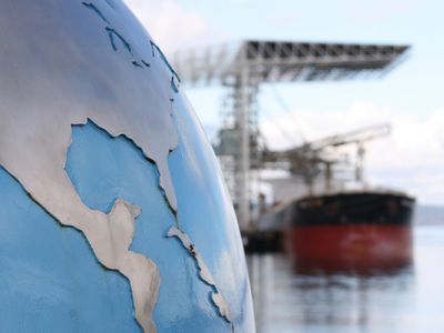 A globe with focus on the United States (USA) and Central America contrasted against a blurred background of a bulk cargo ship.