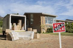 "Sold" sign and moving van filled with cardboard boxes outside a house