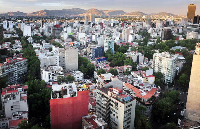 Aerial view of Mexico City with high rise buildings and mountains in the distance.