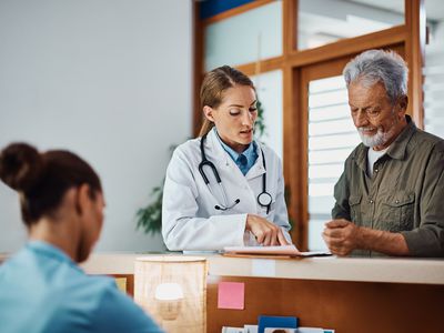 Female doctor going through medical record of senior patient at reception desk