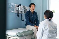 Asian man sitting on an exam table speaking to his doctor