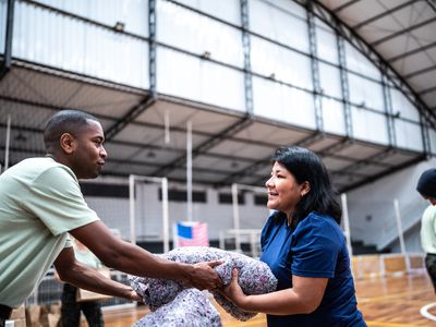 A soldier hands a woman a blanket in a gymnasium. 