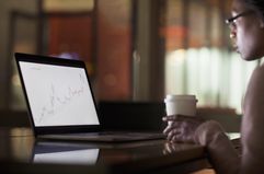 A person looks at a stock chart on a laptop while holding a coffee cup
