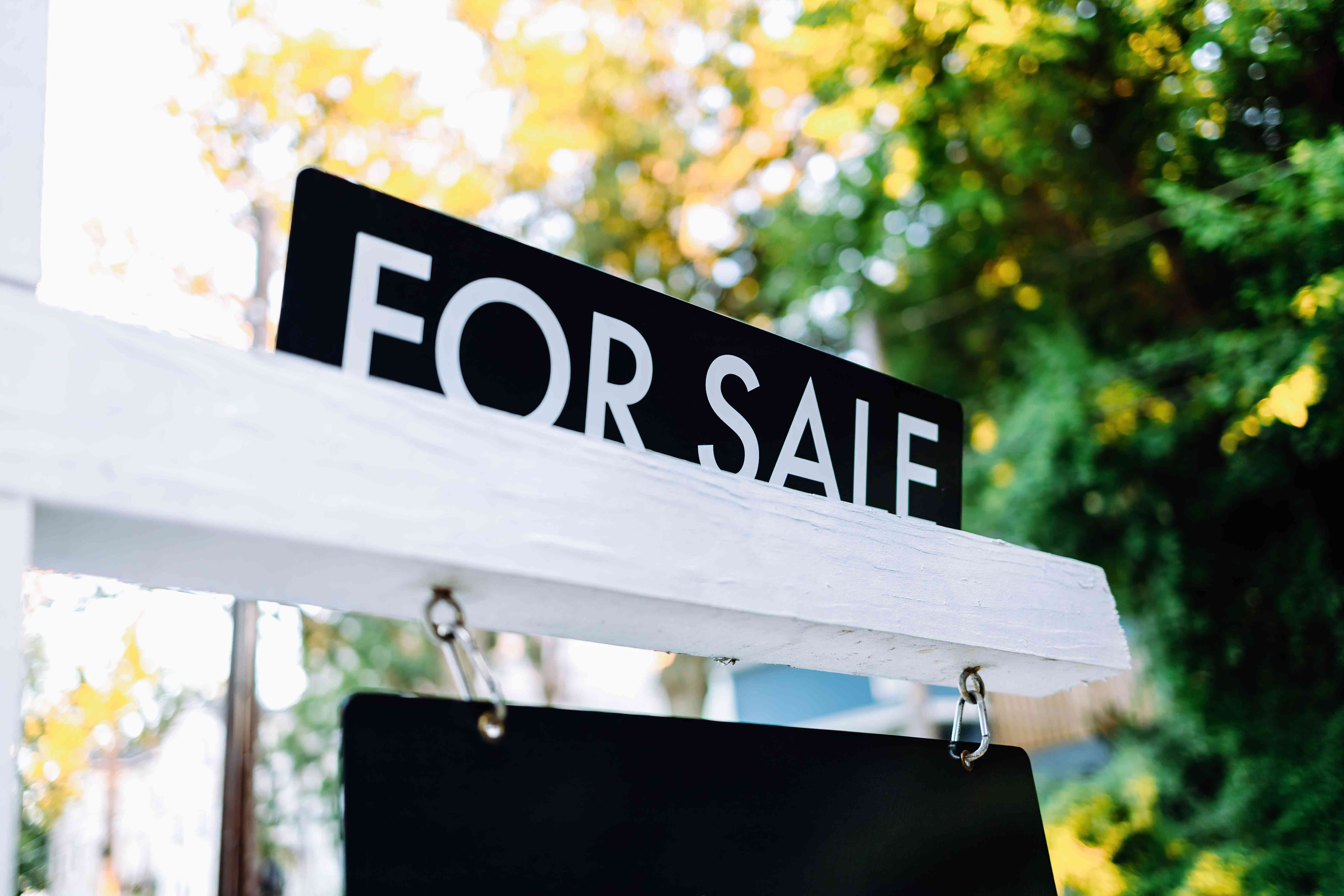 Close-up of for sale rider on real estate sign post in front yard of house