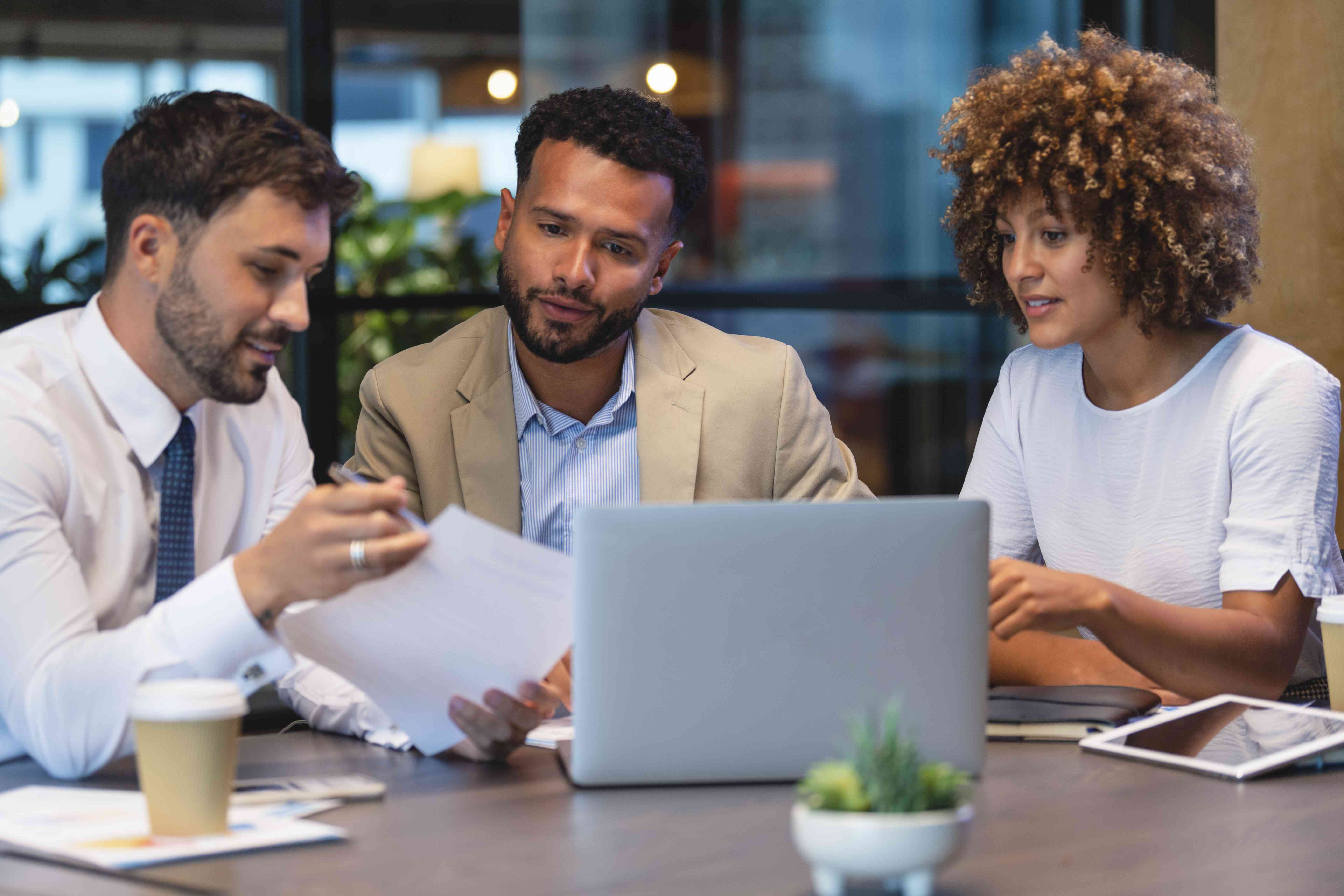 Two business partners meet with an insurance broker at a table to discuss different coverage options.