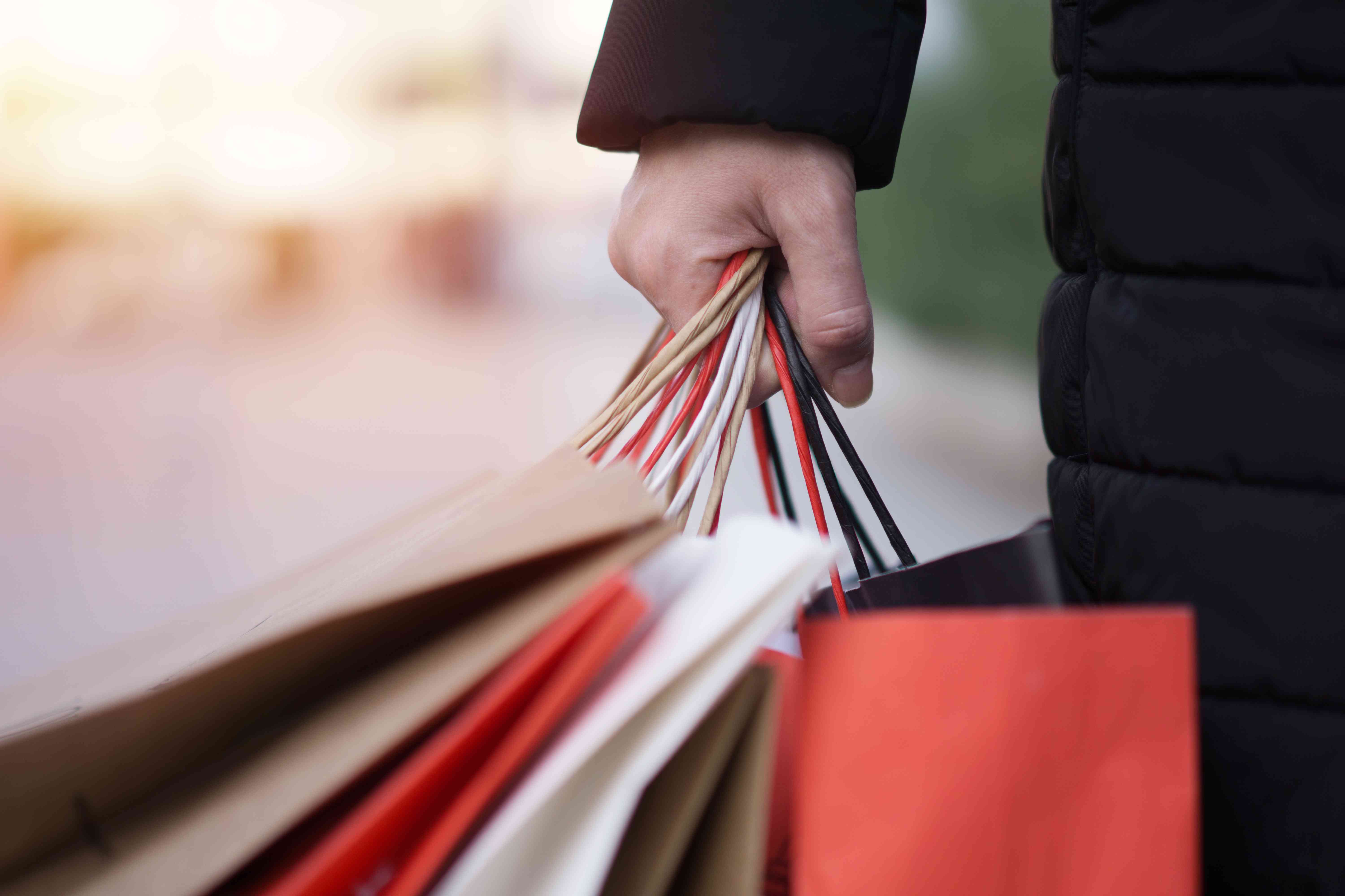 Close up of a person holding five paper bags in their hand while wearing a coat