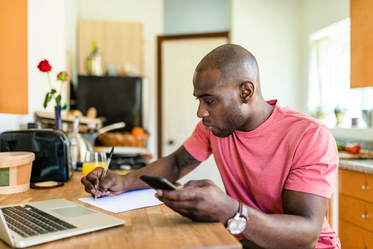 Man at laptop with mobile phone, pen, paper